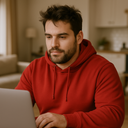 mężczyzna plus size, który będąc w domu, szuka przez interent odzieży męskiej, ubrany w czerwoną bluzę